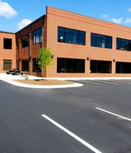 Newly paved commercial parking lot with fresh line striping in front of a modern brick office building with large windows.