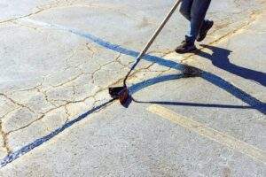 Worker applying crack sealant to a worn asphalt surface, filling long pavement cracks to prevent further damage and extend the lifespan of the pavement.