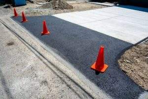 New asphalt driveway replacement in North Carolina featuring freshly paved blacktop connected to a newly poured concrete driveway apron, with orange safety cones marking the surface during installation.
