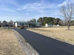 Long residential asphalt driveway installation for a rural home featuring an extended curved layout and professional grading compaction.
