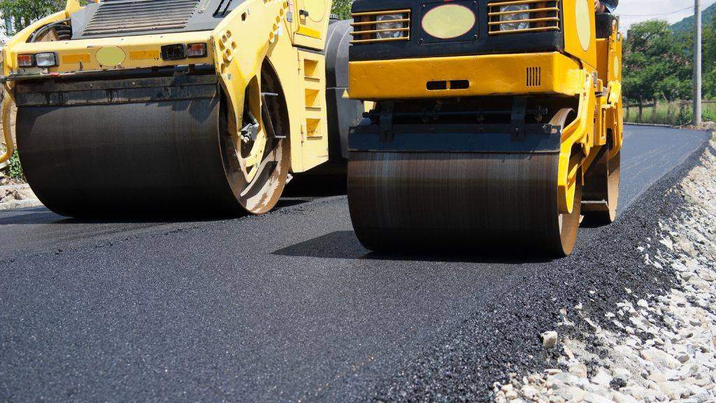 Heavy heavy-duty asphalt compaction rollers smoothing fresh hot-mix asphalt during a fall driveway paving project.
