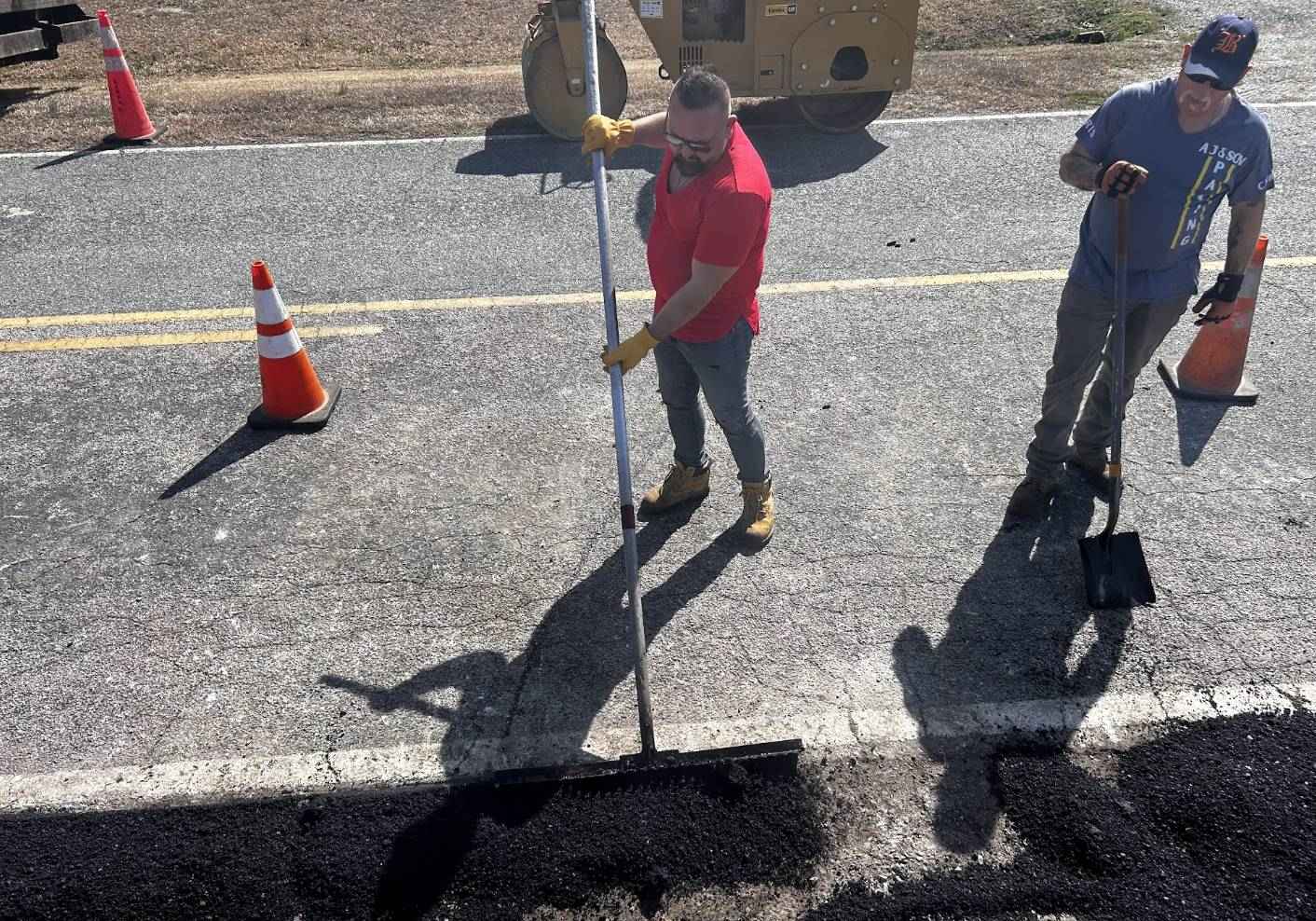 Paving crew spreading and preparing hot-mix asphalt for road repairs.