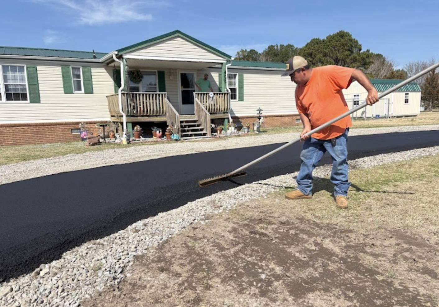 A.J. & Son Asphalt Paving worker using a asphalt rake to level hot blacktop along a residential driveway.
