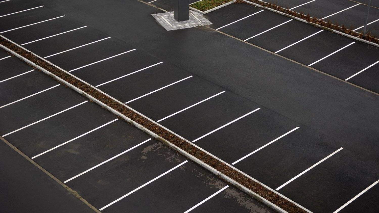 cracked commercial parking lot with worn striping before fall resurfacing 
